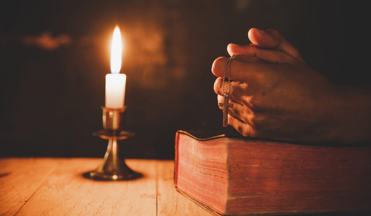 Close up man's hand is praying in the Church with lit candle, religion and faith concept