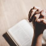 Spirituality and religion, Hands folded in prayer on a Holy Bibl Spirituality and religion, Hands folded in prayer on a Holy Bible in church concept for faith.