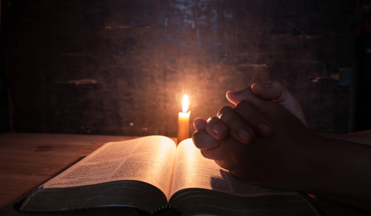 women praying on the Bible in the light candles selective focus. Beautiful gold background. Religion concept.